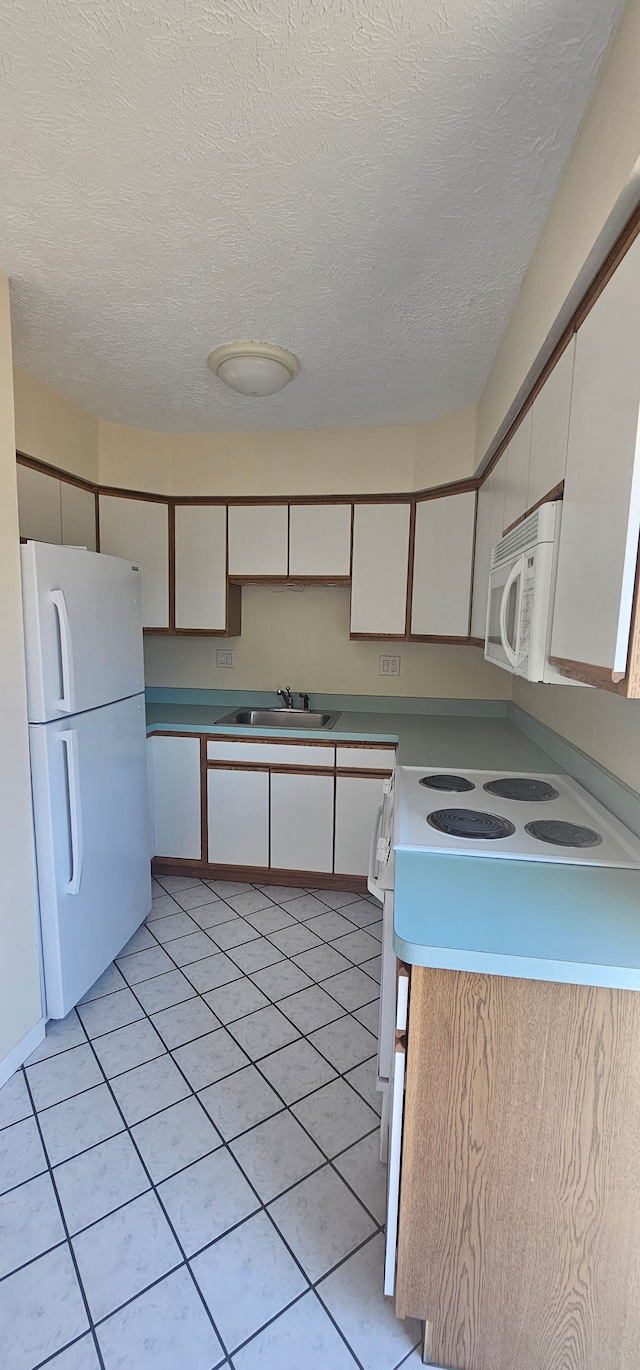 kitchen with white appliances, light tile patterned floors, a sink, a textured ceiling, and white cabinetry