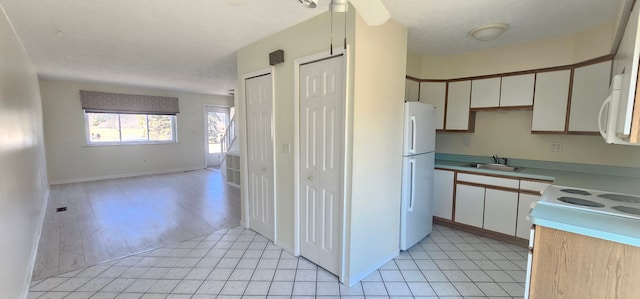 kitchen with open floor plan, light countertops, light tile patterned floors, white appliances, and a sink