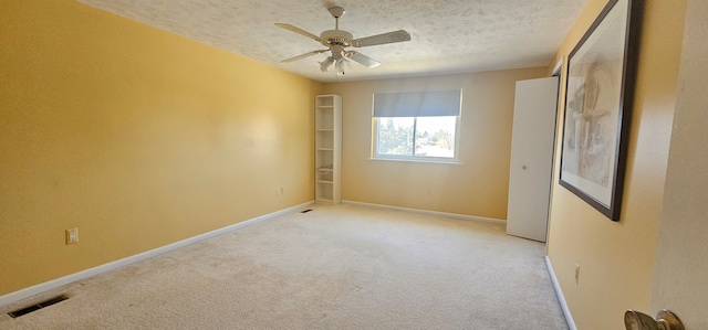 spare room featuring a textured ceiling, a ceiling fan, baseboards, visible vents, and light carpet