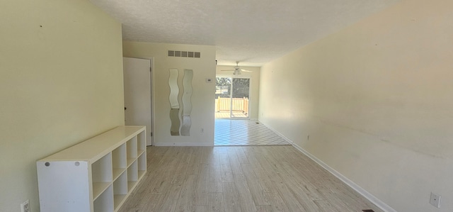 corridor with baseboards, visible vents, a textured ceiling, and light wood-style floors