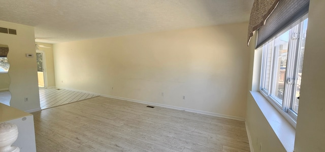 unfurnished living room featuring visible vents, baseboards, a textured ceiling, and light wood finished floors