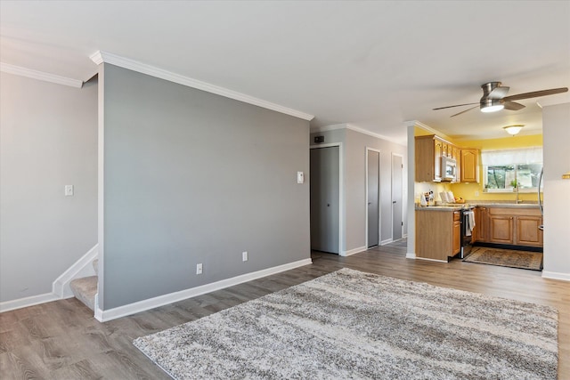 kitchen featuring crown molding, baseboards, wood finished floors, stainless steel appliances, and a sink