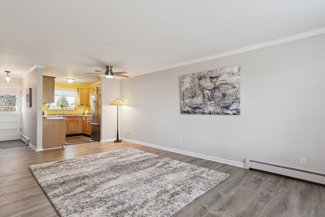 living area with a baseboard heating unit, wood finished floors, baseboards, and ornamental molding