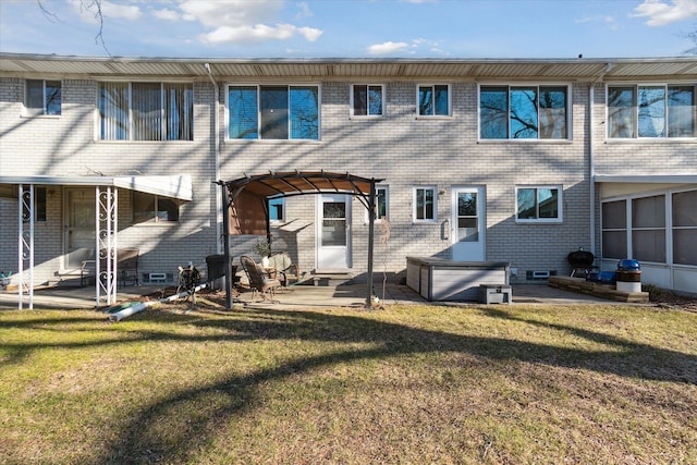 back of house with brick siding, a lawn, a hot tub, and a patio