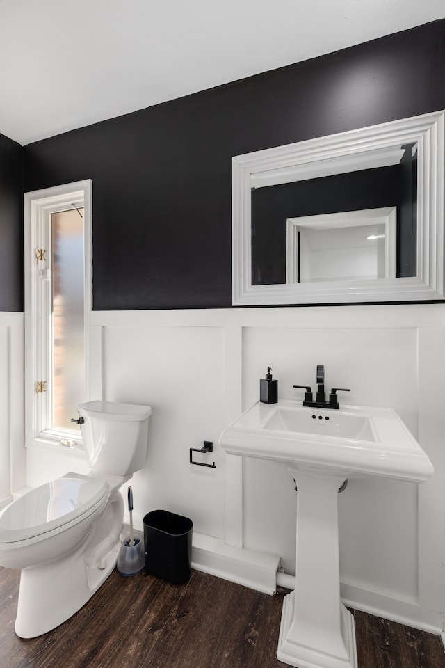 bathroom featuring a sink, toilet, wood finished floors, and wainscoting