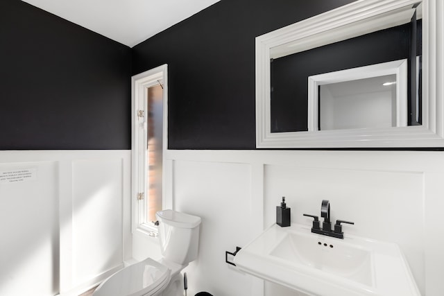 bathroom featuring a decorative wall, toilet, a wainscoted wall, and a sink