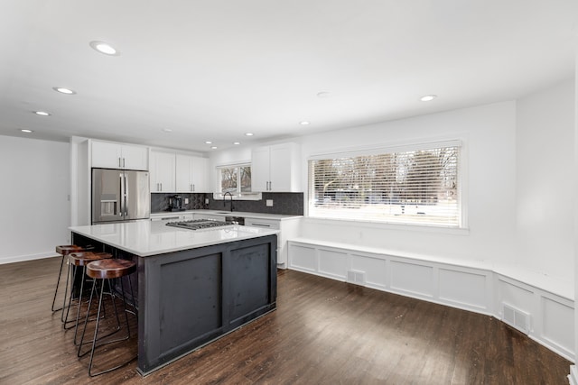 kitchen with visible vents, stainless steel appliances, decorative backsplash, white cabinets, and a center island