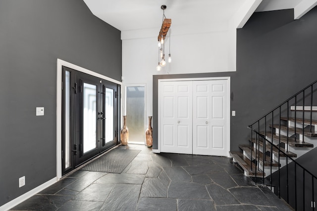 foyer featuring stone tile flooring, french doors, baseboards, a towering ceiling, and stairs