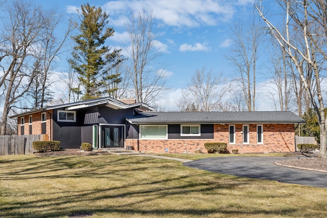 mid-century modern home featuring brick siding, a front lawn, and fence