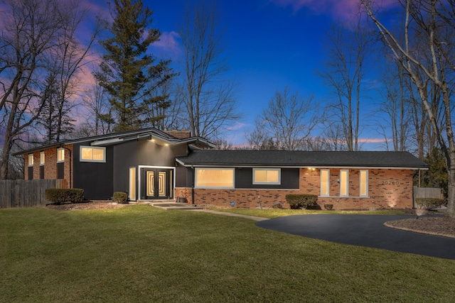 mid-century inspired home featuring fence, a yard, french doors, aphalt driveway, and brick siding