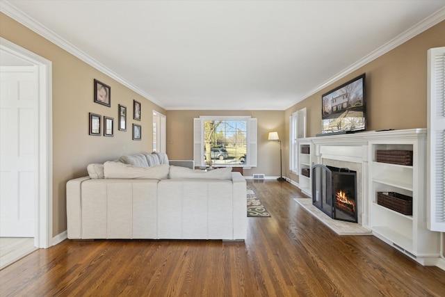 living area with visible vents, baseboards, dark wood-style flooring, a lit fireplace, and crown molding