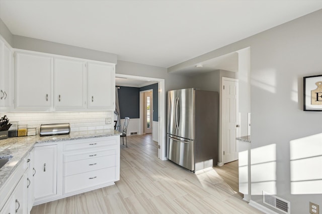 kitchen with visible vents, light stone counters, decorative backsplash, freestanding refrigerator, and white cabinets