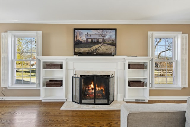 interior details with visible vents, crown molding, baseboards, a warm lit fireplace, and wood finished floors