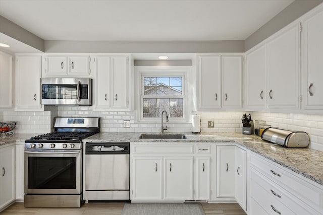 kitchen featuring a sink, light stone countertops, appliances with stainless steel finishes, and white cabinets