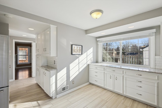 kitchen featuring tasteful backsplash, visible vents, white cabinets, and light stone countertops