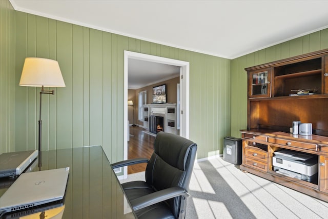 carpeted home office featuring baseboards, a warm lit fireplace, and crown molding