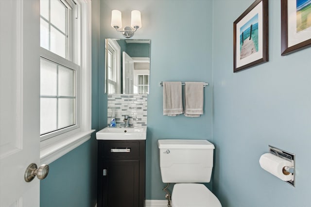 half bath featuring toilet, plenty of natural light, vanity, and tasteful backsplash