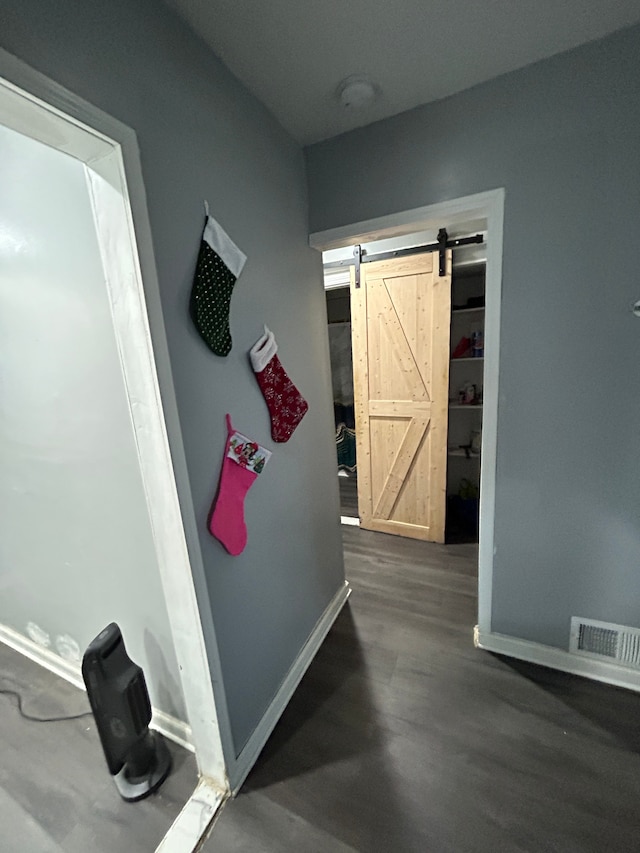 corridor with a barn door, baseboards, dark wood-type flooring, and visible vents