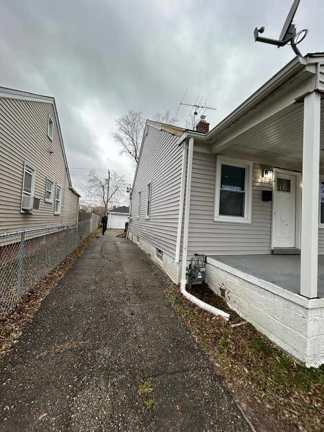 view of side of home featuring fence, a porch, cooling unit, a chimney, and an outdoor structure