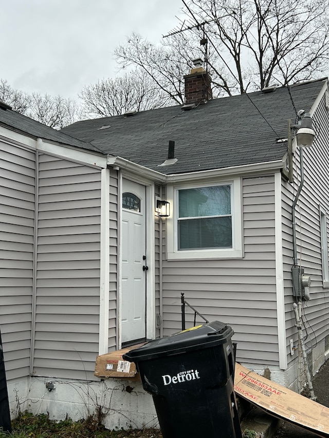 entrance to property with a chimney and a shingled roof