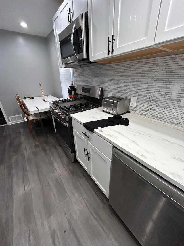 kitchen featuring visible vents, backsplash, dark wood-type flooring, light stone counters, and appliances with stainless steel finishes