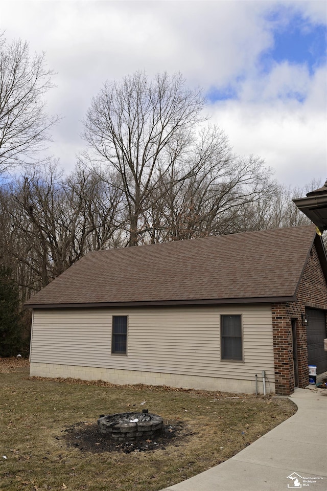 view of property exterior with a garage, a fire pit, brick siding, and a shingled roof