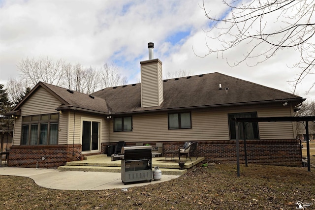 rear view of property with a patio, brick siding, roof with shingles, and a chimney