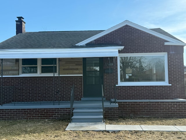 view of front of property featuring a chimney, brick siding, and a shingled roof