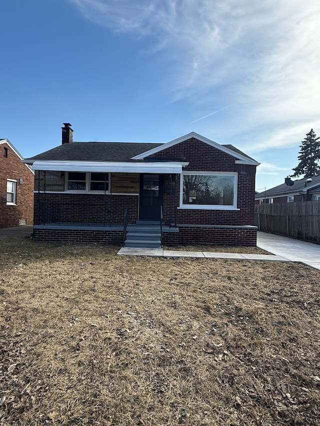 view of front of home featuring brick siding, a porch, a front lawn, and fence