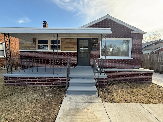 bungalow featuring fence, covered porch, and brick siding