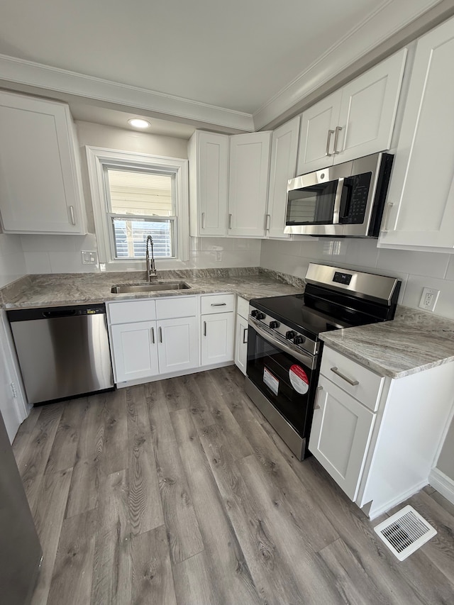 kitchen featuring visible vents, a sink, white cabinets, light wood-style floors, and appliances with stainless steel finishes