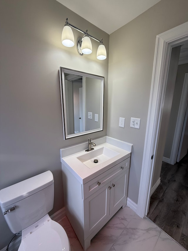 half bath featuring baseboards, toilet, marble finish floor, and vanity