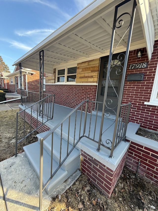 view of exterior entry with brick siding and covered porch