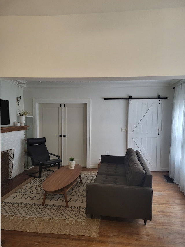 living room with light wood-style flooring, a brick fireplace, crown molding, and a barn door