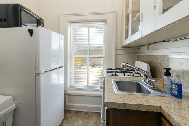 kitchen featuring light countertops, white cabinets, glass insert cabinets, and freestanding refrigerator