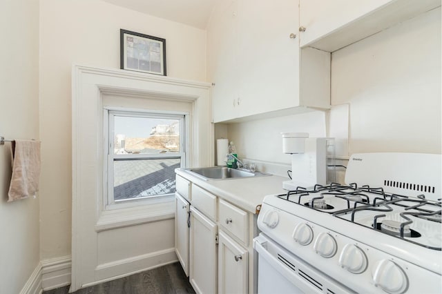 kitchen featuring a sink, light countertops, baseboards, white gas range, and dark wood-style flooring