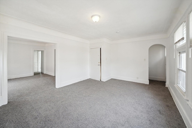 unfurnished room with baseboards, arched walkways, and dark carpet