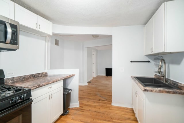 kitchen featuring black gas range oven, a sink, white cabinetry, stainless steel microwave, and light wood-type flooring