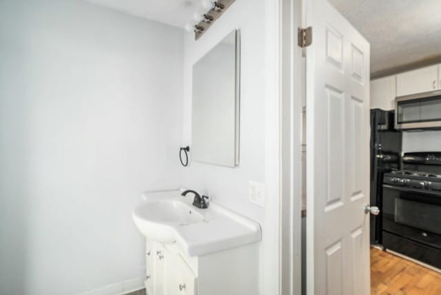 bathroom with vanity, wood finished floors, baseboards, and a textured ceiling