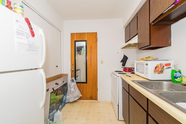 kitchen featuring under cabinet range hood, white appliances, light floors, and a sink