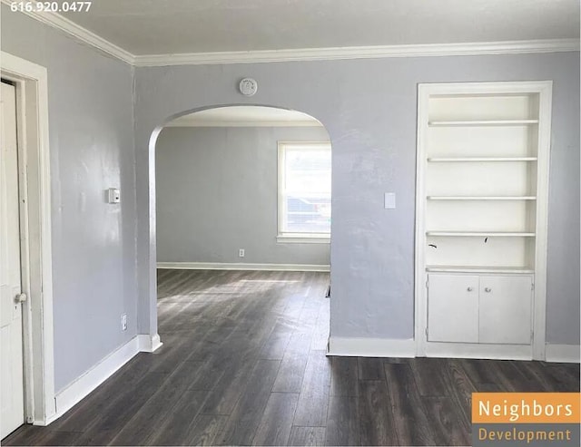 empty room with built in features, dark wood finished floors, arched walkways, crown molding, and baseboards