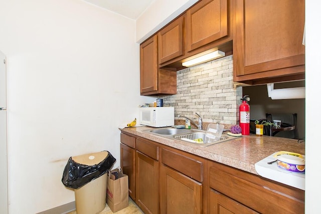 kitchen with a sink, tasteful backsplash, brown cabinetry, light countertops, and white microwave