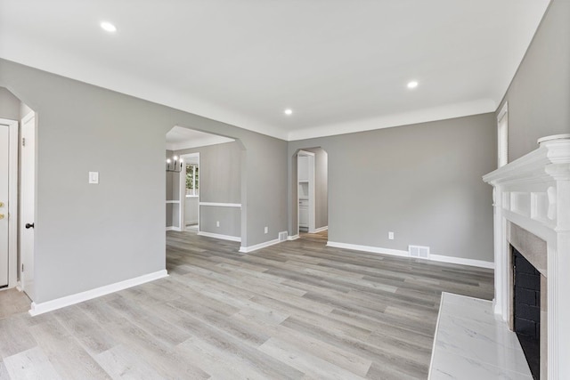 unfurnished living room featuring light wood-style floors, a fireplace with flush hearth, baseboards, and arched walkways