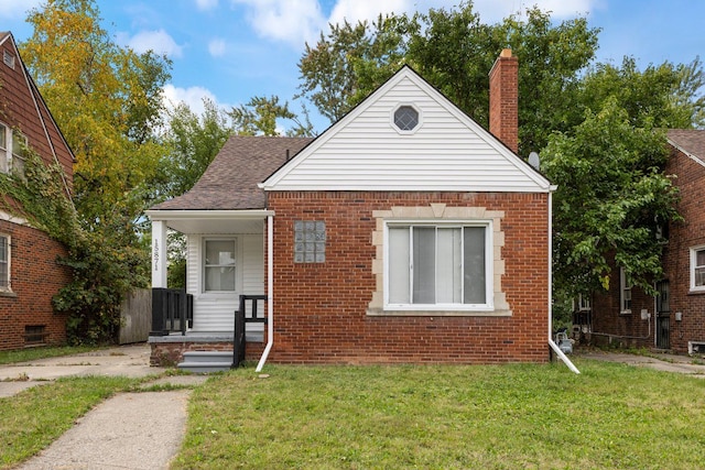 bungalow-style house featuring brick siding, a chimney, a front yard, and roof with shingles