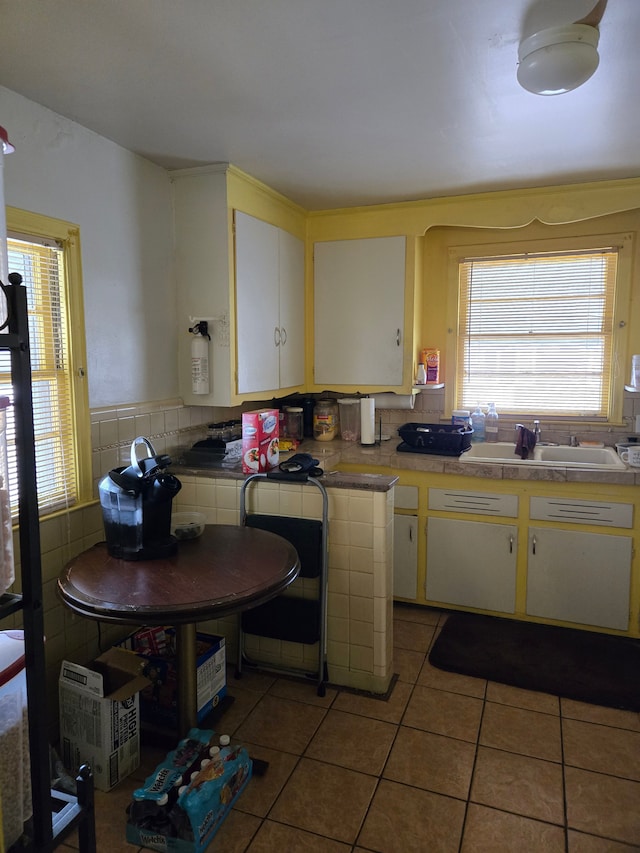 kitchen with tile countertops, light tile patterned floors, wainscoting, white cabinets, and a sink