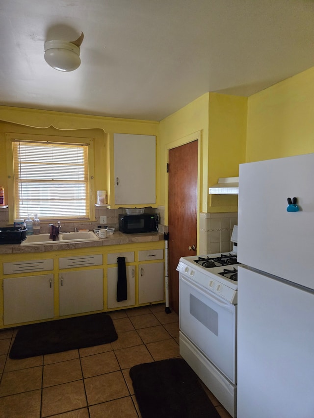 kitchen featuring backsplash, under cabinet range hood, light tile patterned floors, white appliances, and a sink