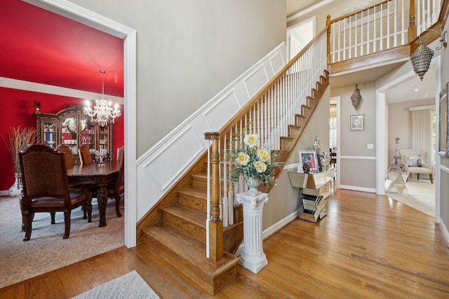 staircase with a high ceiling, a decorative wall, wood finished floors, and a chandelier