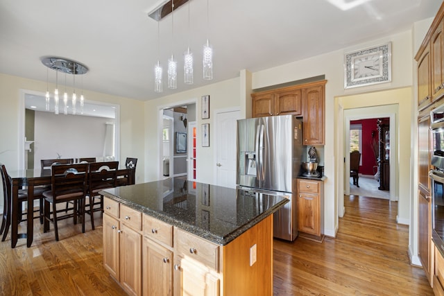 kitchen with dark stone counters, light wood-style floors, stainless steel refrigerator with ice dispenser, and a kitchen island