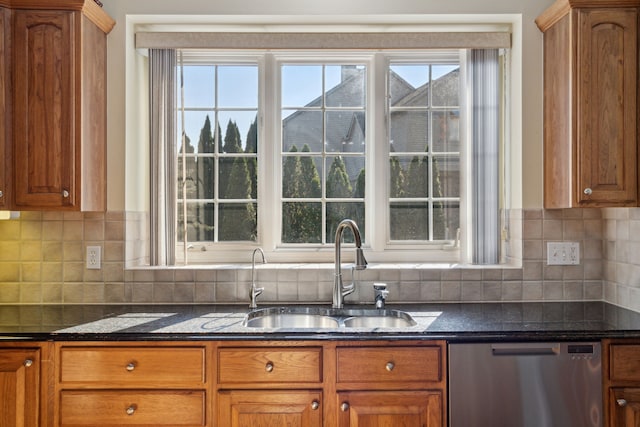 kitchen featuring dark stone counters, decorative backsplash, stainless steel dishwasher, brown cabinetry, and a sink