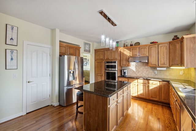 kitchen featuring backsplash, a center island, under cabinet range hood, light wood-style flooring, and appliances with stainless steel finishes